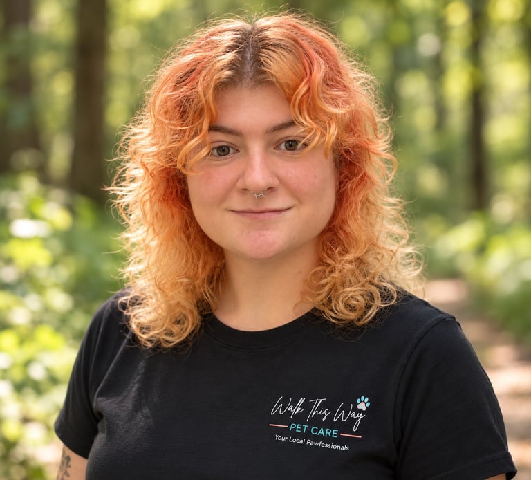 Woman with curly orange hair wearing a black t-shirt, smiling at the camera with a blurred forest background
