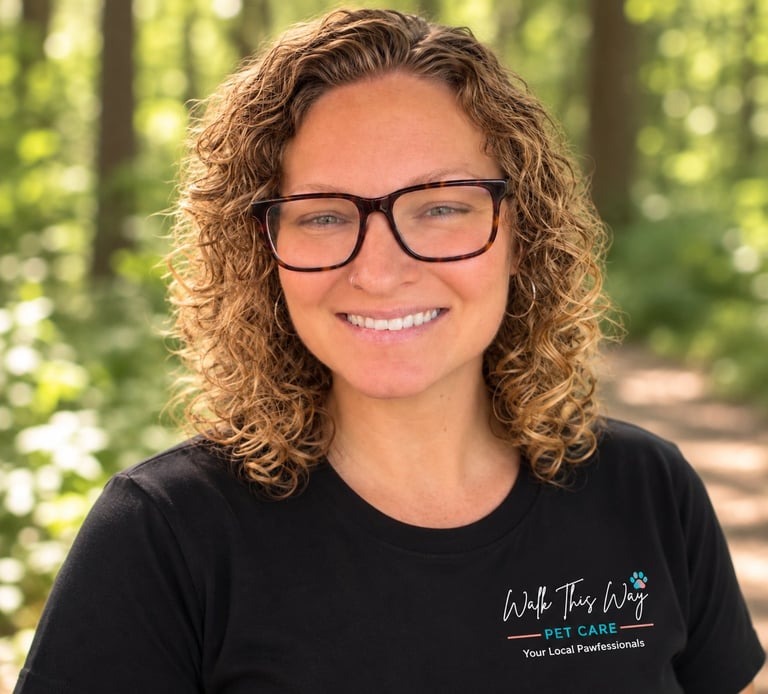 Woman with curly brown hair and glasses smiling outdoors, wearing a black Walk This Way Pet Care t-shirt