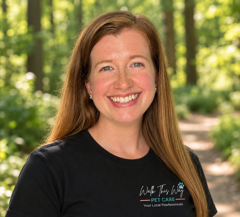 Smiling woman with long reddish-brown hair wearing a black pet care t-shirt, photographed outdoors with a forested background